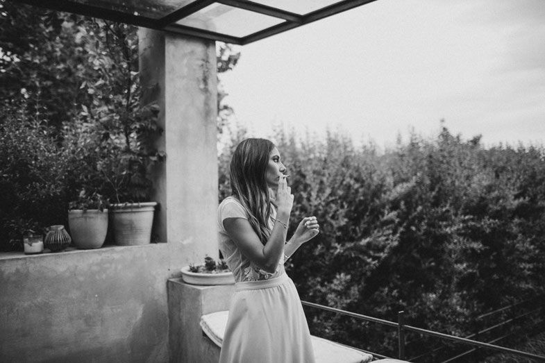 A person in a white dress sits on a balcony overlooking a forested landscape.