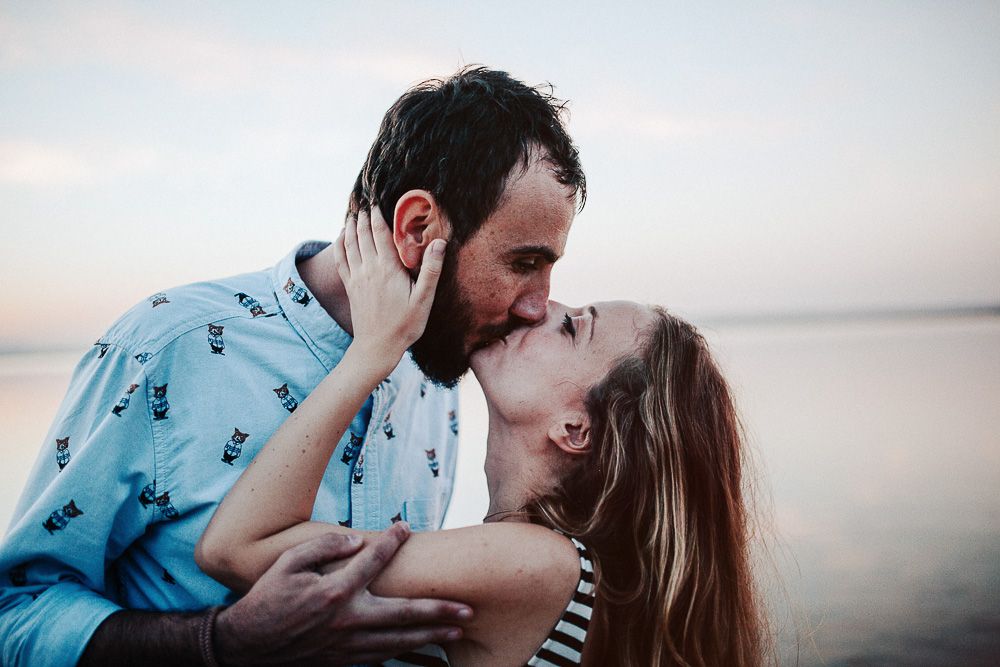 A romantic couple shares an intimate moment at sunset by the water.