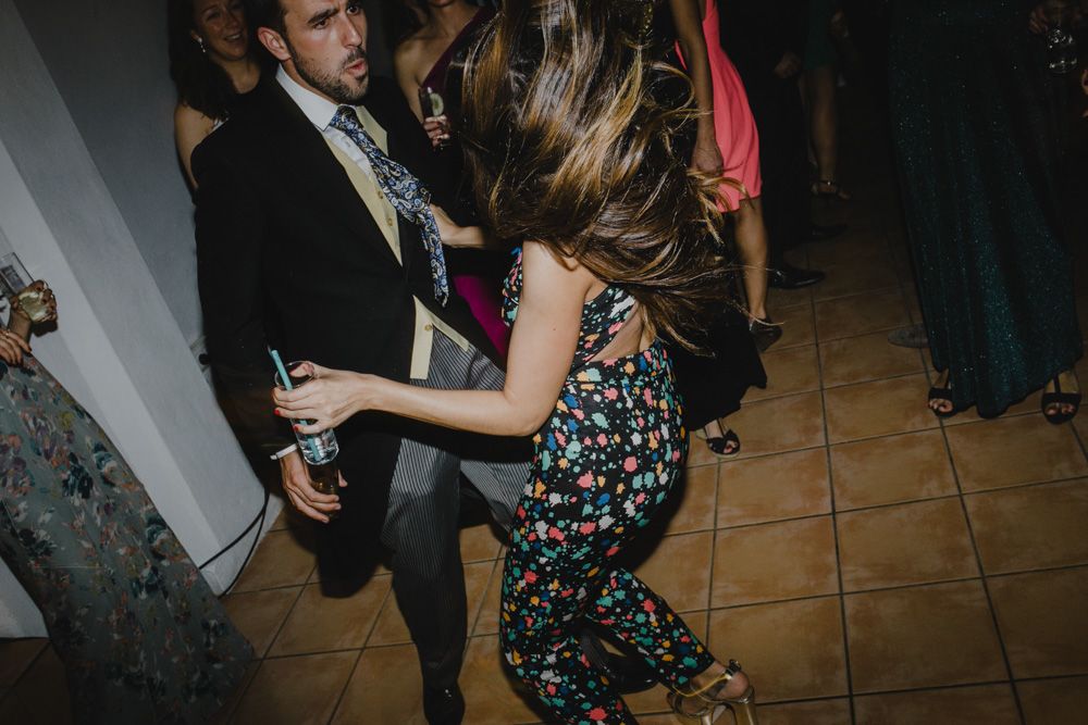 Wedding guests dancing energetically on a tiled floor at a reception party.