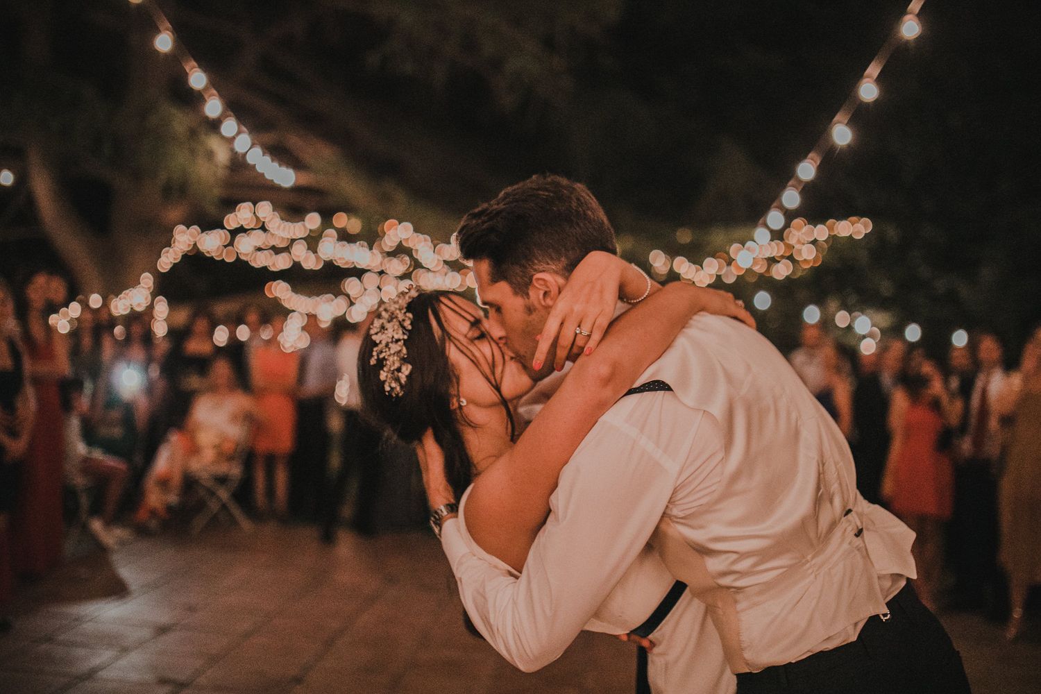 A romantic dance under string lights at an outdoor wedding reception.