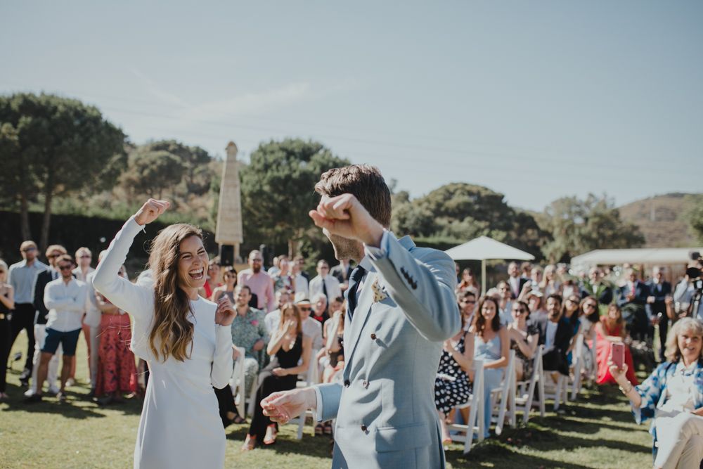 Joyful couple raises arms in celebration during outdoor wedding ceremony.