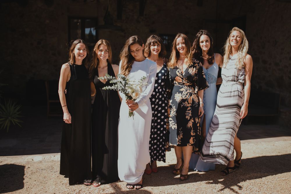 A group of women in formal dresses posing together at an outdoor wedding ceremony.