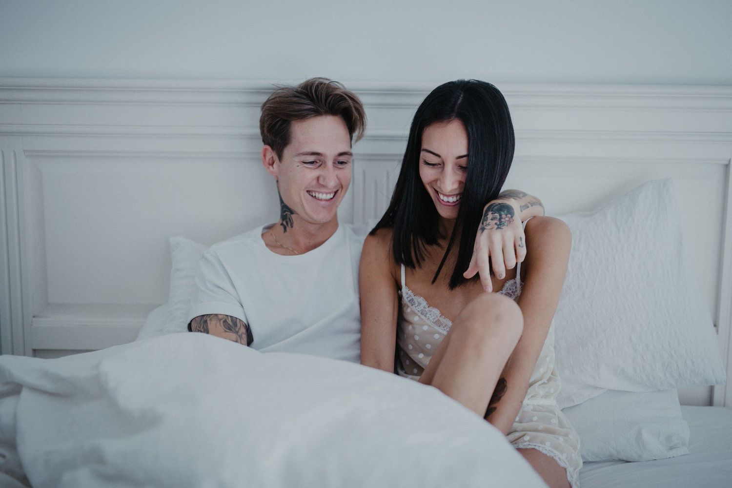 A couple sharing an intimate moment while relaxing together in bed wearing white.