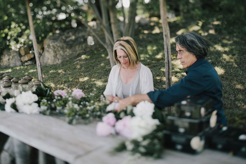 Two people arrange delicate white and pink flowers at an outdoor table.