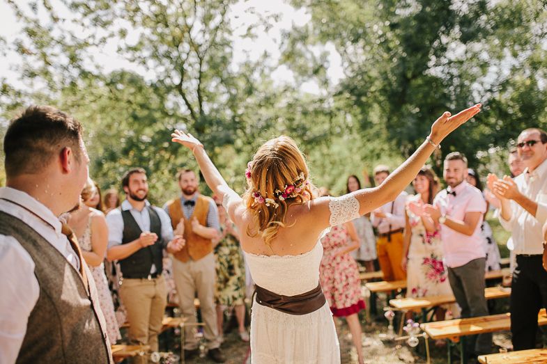 A celebratory moment at an outdoor wedding with guests cheering under tree canopy.