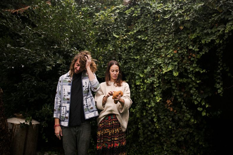 Two people share an intimate moment against greenery in an outdoor setting.