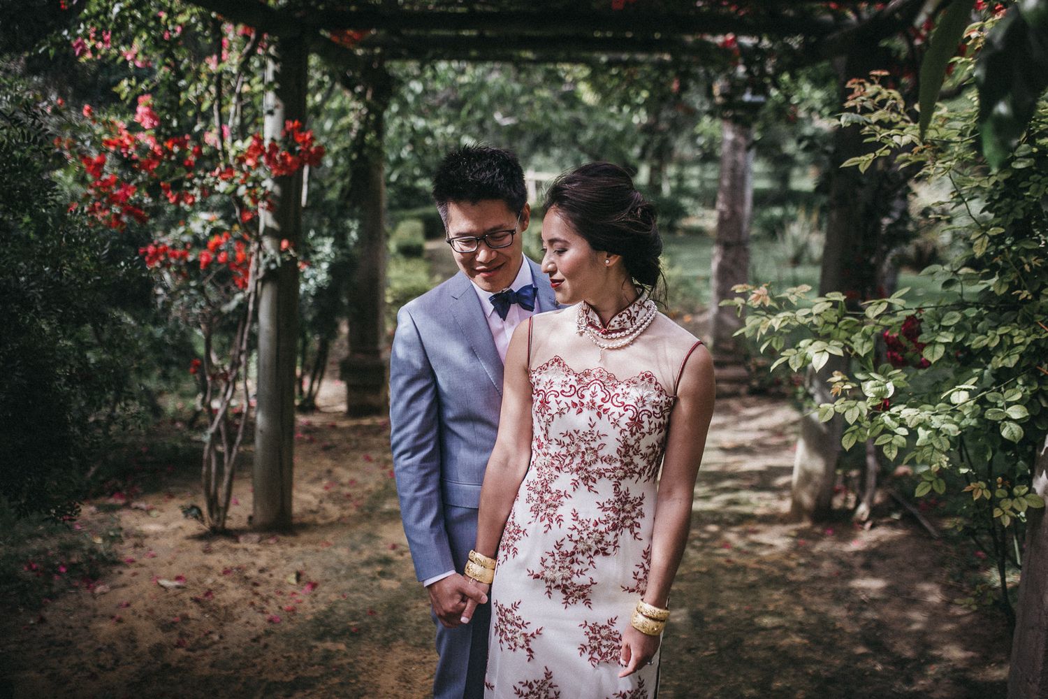 Couple in formal attire posing under garden arbor with floral details.