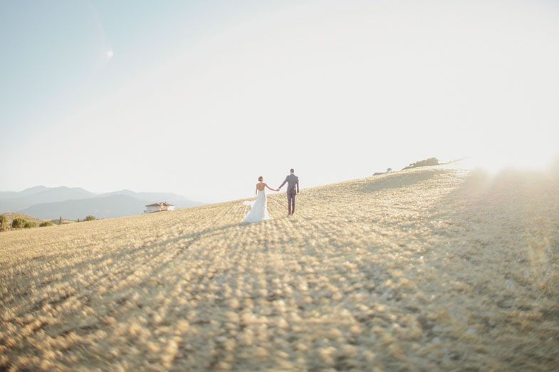 Two figures walking hand in hand across a sunlit hilltop with mountains in the background.
