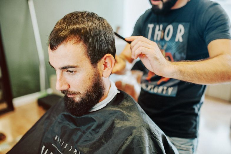 Barber trimming hair with scissors in a modern barbershop setting.