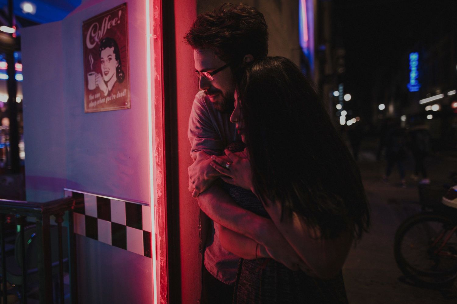 A couple sharing a romantic moment under red neon lights at night.