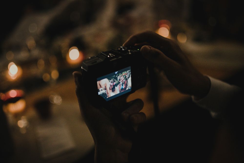 Silhouetted hands hold up a phone to capture photos at a nighttime event.
