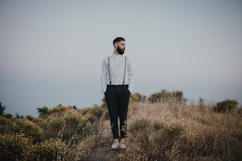 Person in casual attire with suspenders standing in field during golden hour.