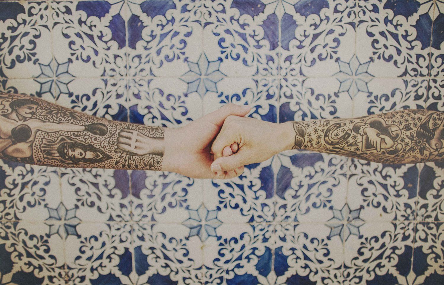 Intricately decorated henna hands holding together against blue and white patterned background.