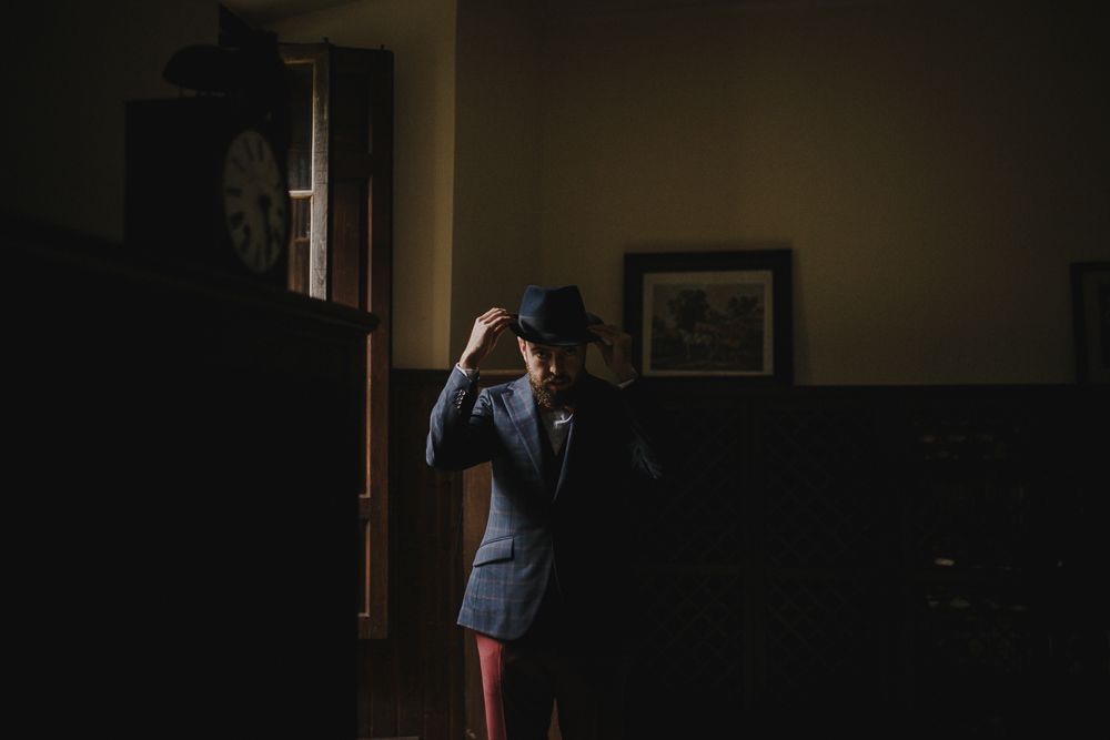Figure in formal wear stands dramatically lit in dark interior space.