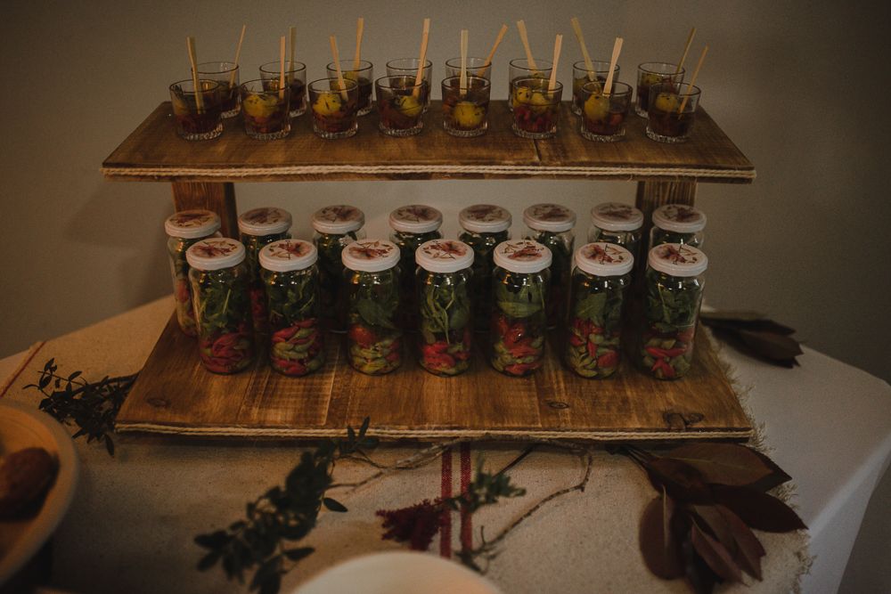Two-tiered wooden display stand with mason jar drinks and appetizers at a wedding reception.