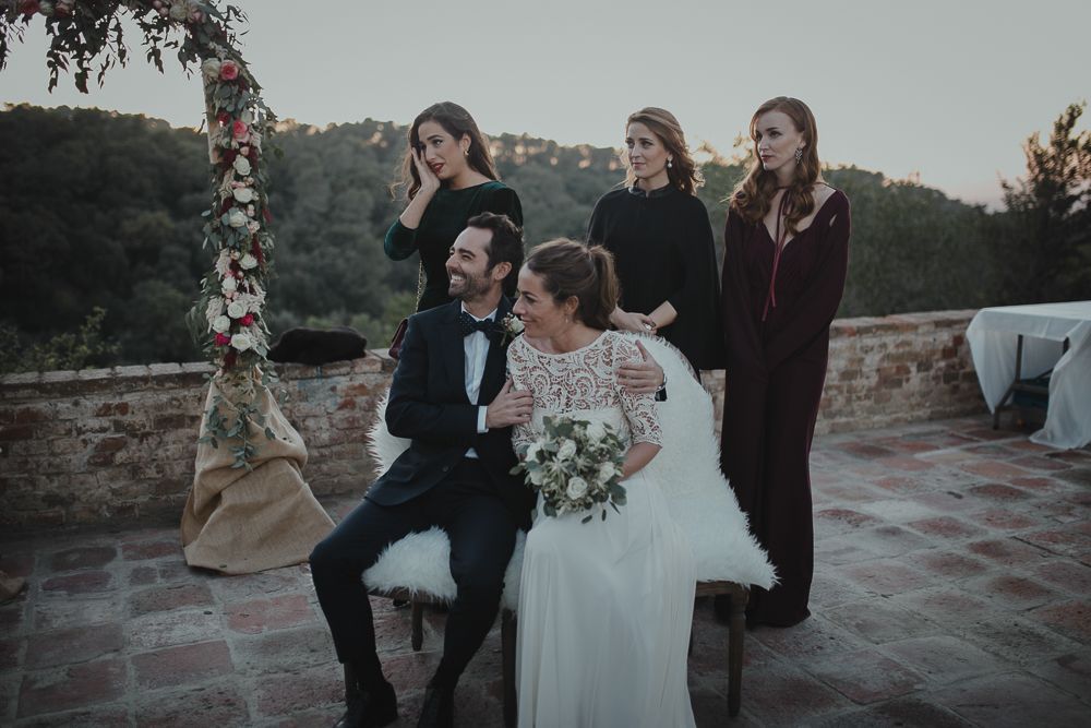Wedding party posing under floral arch at sunset.
