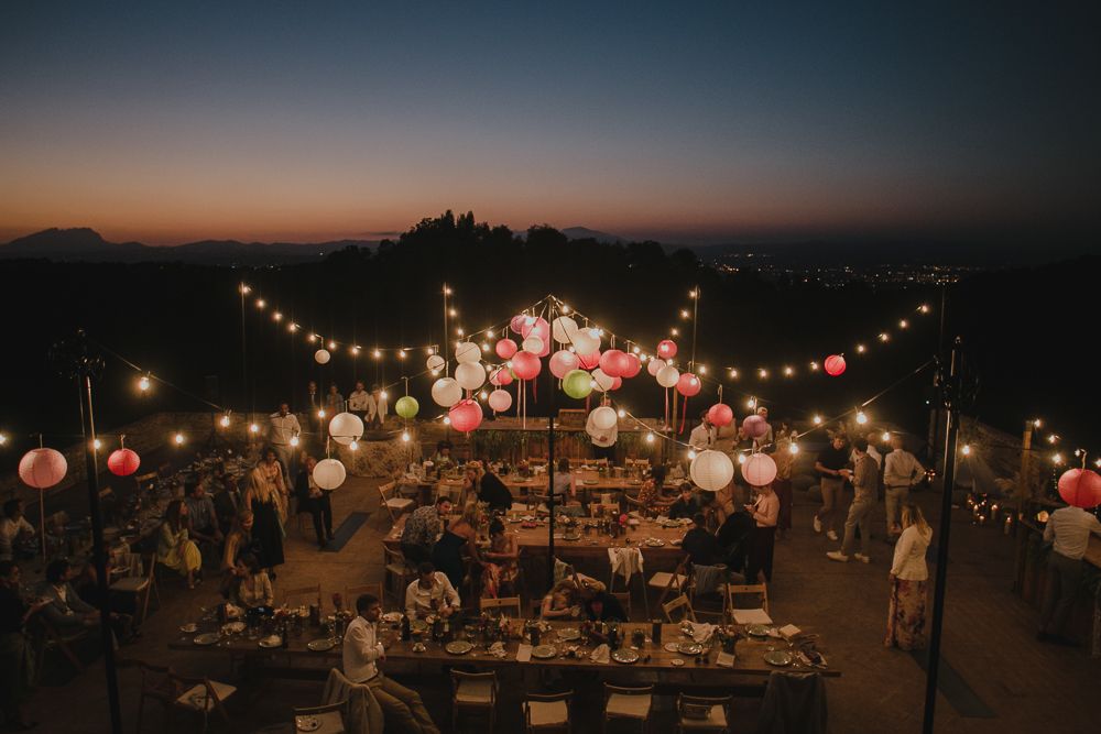Outdoor wedding reception at sunset with hanging lanterns and string lights creating a magical atmosphere.