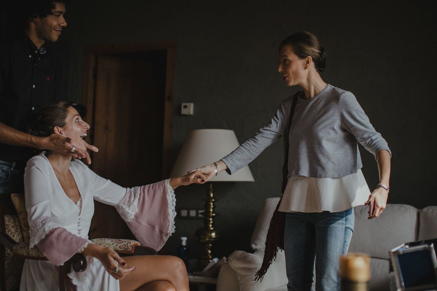 Two people interact playfully during wedding preparations in a dimly lit room.