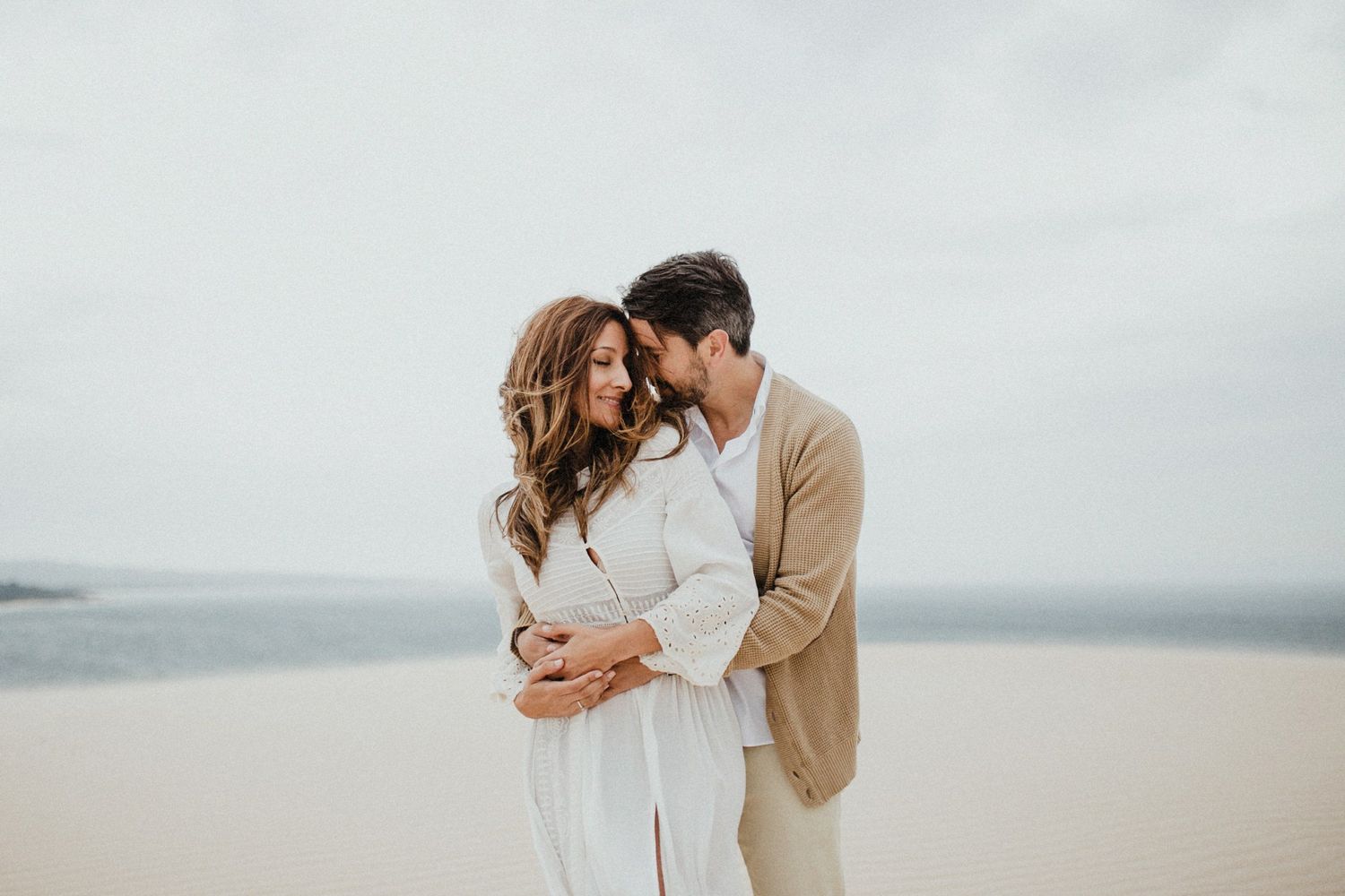 Intimate couple moment captured on misty sand dunes in soft natural light.
