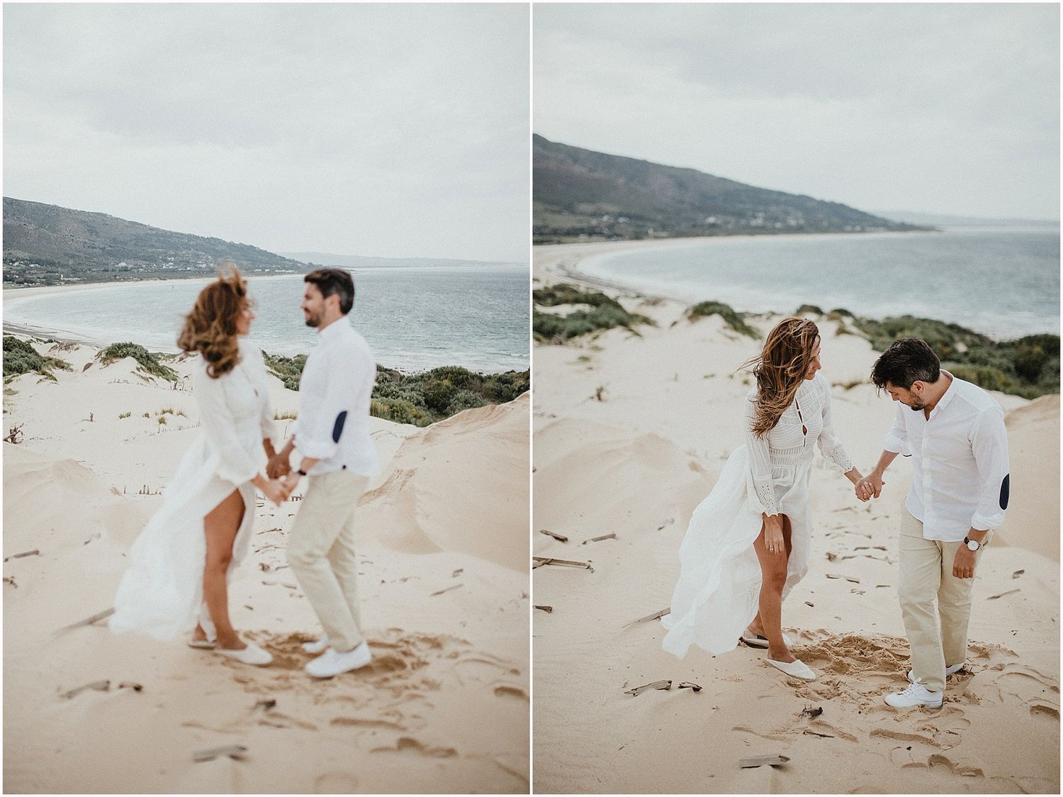 Playful couple in white clothing dancing together on a coastal beach.