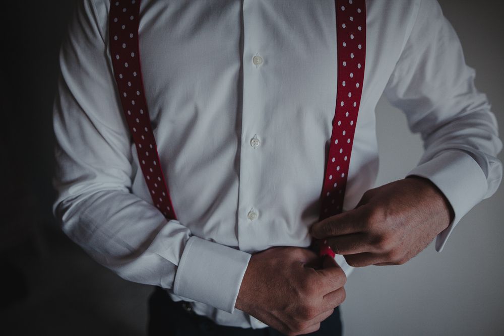 Person wearing white dress shirt and red polka dot suspenders adjusting their outfit.