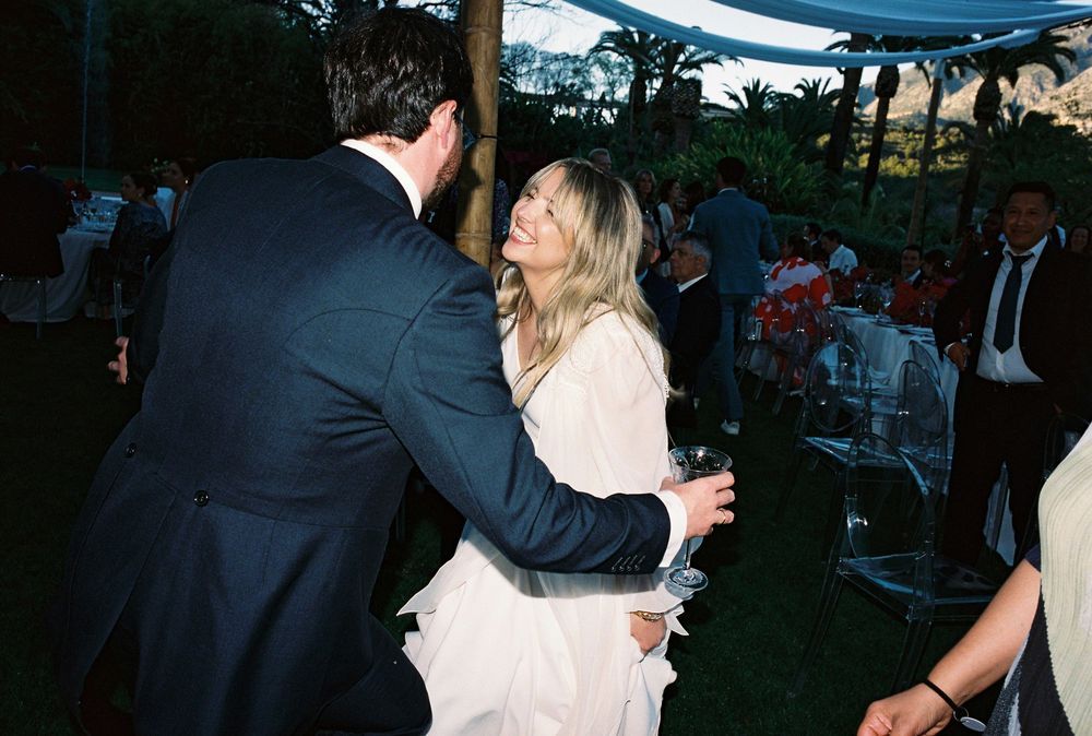 Wedding party dancing together outdoors at dusk during reception celebration.