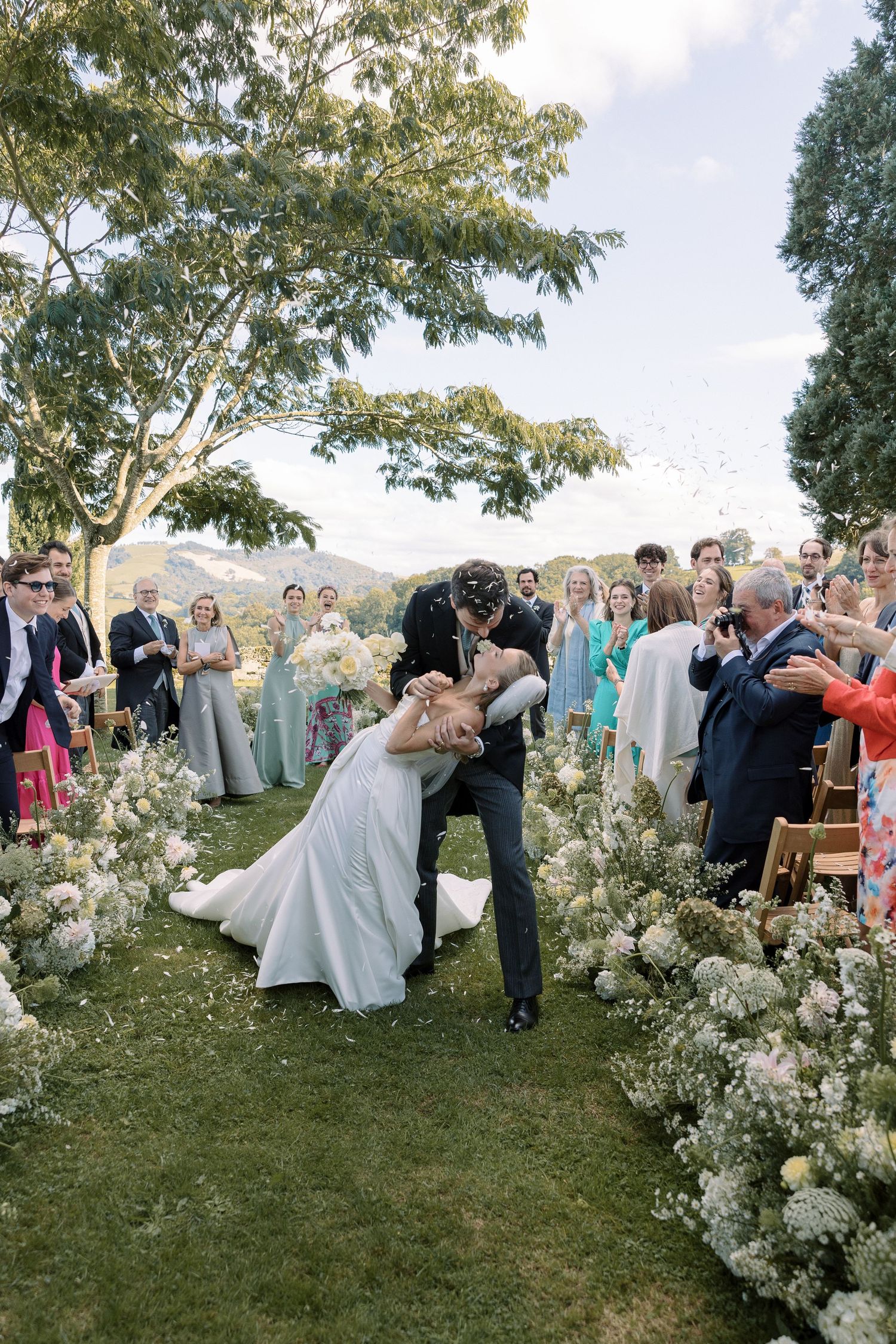 Outdoor garden wedding celebration with white floral arrangements and guests dancing.