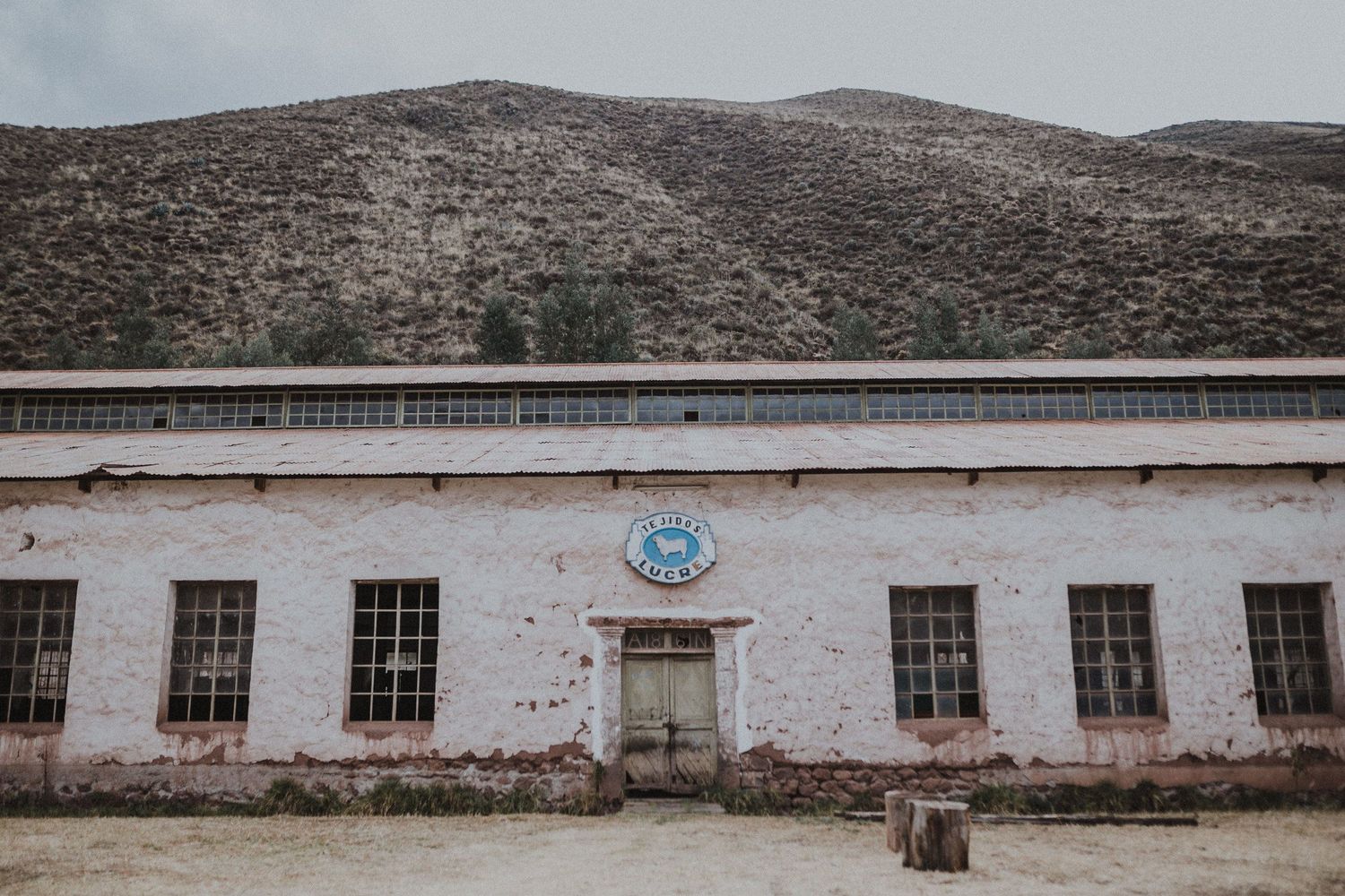 Old white institutional building with blue emblem and symmetrical windows in mountainous terrain.