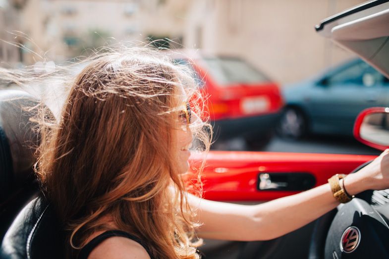 Woman with windswept hair reaching out from a red convertible car.