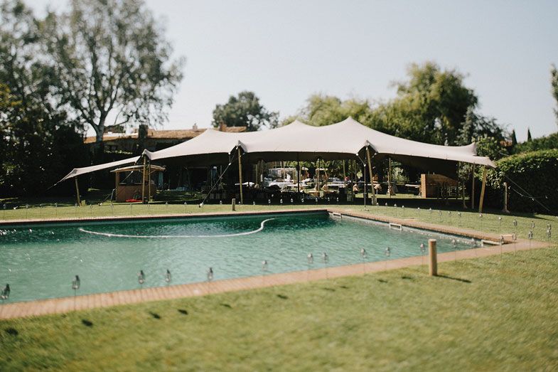 Swimming pool with white canopy tents in a manicured backyard setting.