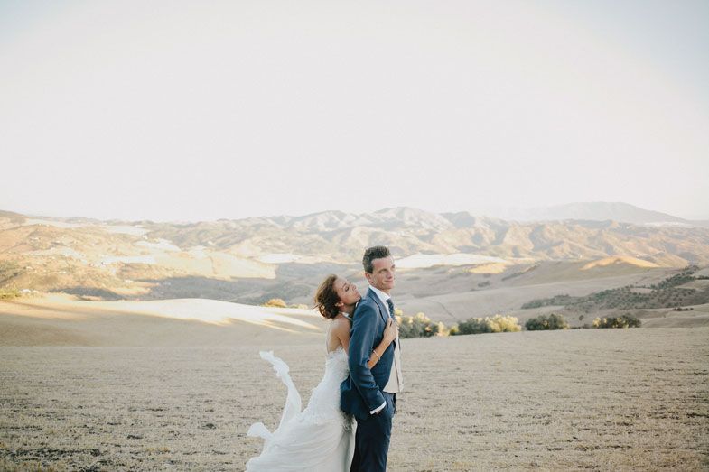 Couple sharing a romantic moment on a winding mountain road with scenic hills in the background.