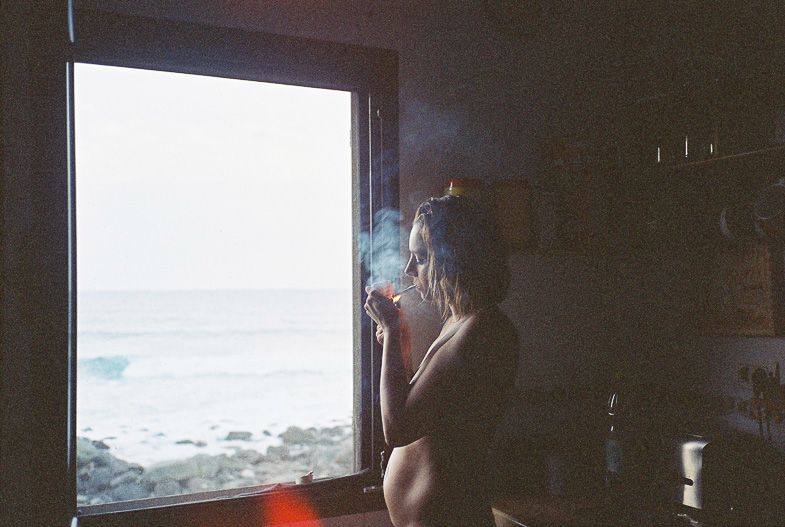 Silhouette by window looking out at ocean view with cigarette smoke drifting.