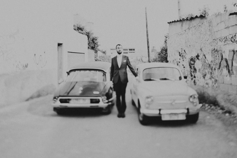 Vintage black and white photo of someone standing between two classic cars on a street.