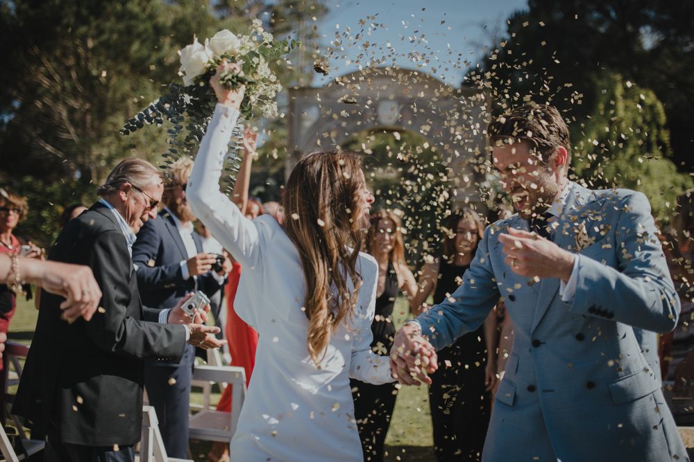 Wedding couple celebrates amid shower of confetti during outdoor reception.