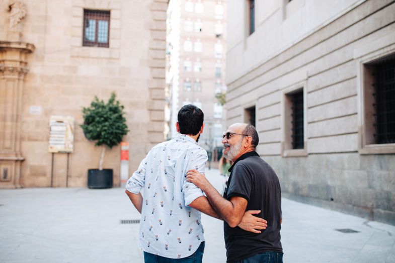 Two people conversing on a street with classical stone buildings in the background.