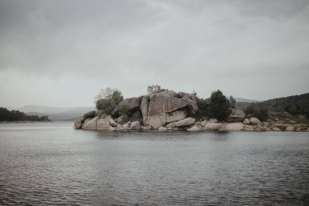 Rocky island formation in a misty lake surrounded by mountains on an overcast day.