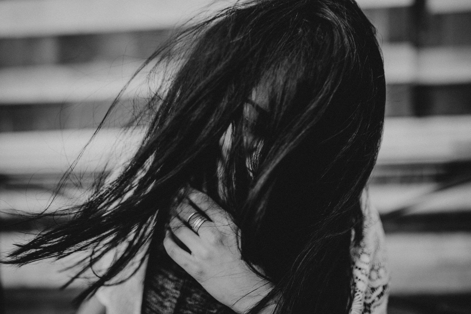 Black and white portrait of long dark hair flowing in motion against window blinds.