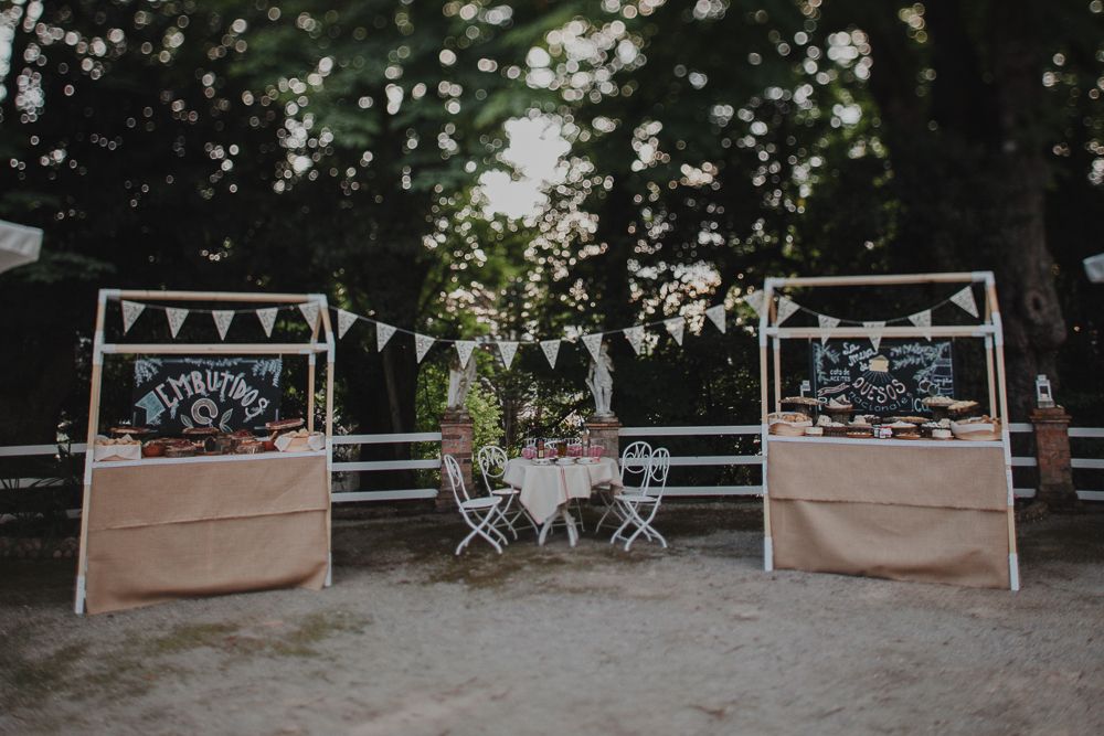 Three outdoor wedding food stations with bunting and white chairs set up in a garden setting.