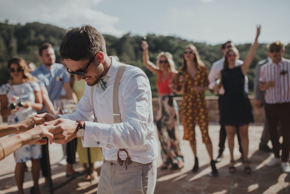 Guest exchanges rings during sunny outdoor wedding ceremony with crowd watching.