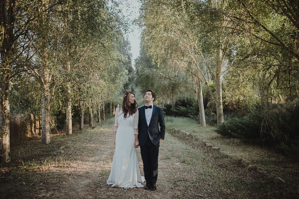 A bride and groom walk together on a tree-lined path during their woodland wedding photoshoot.