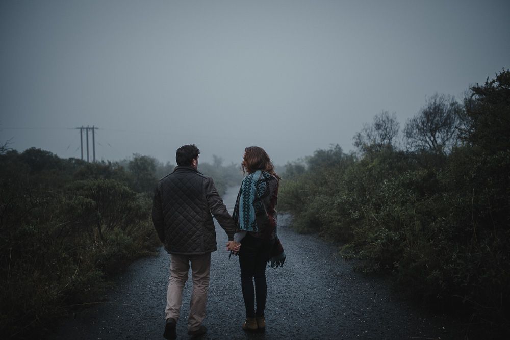 A couple walking hand in hand on a foggy path with power lines visible in the distance.