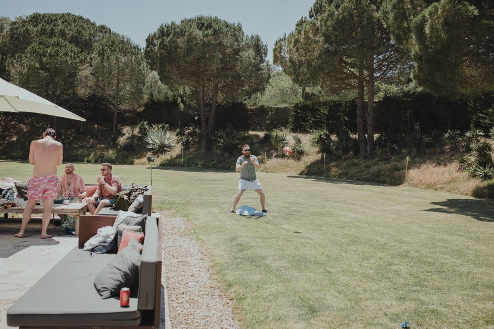 People relax on lounge chairs while someone plays on a grassy lawn area surrounded by trees.