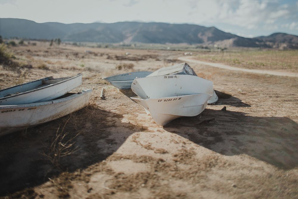 Weathered boats rest on dry desert terrain with mountains in the background.