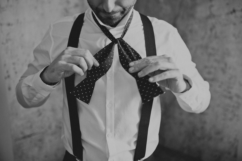 Close-up of hands adjusting a black bowtie with suspenders.