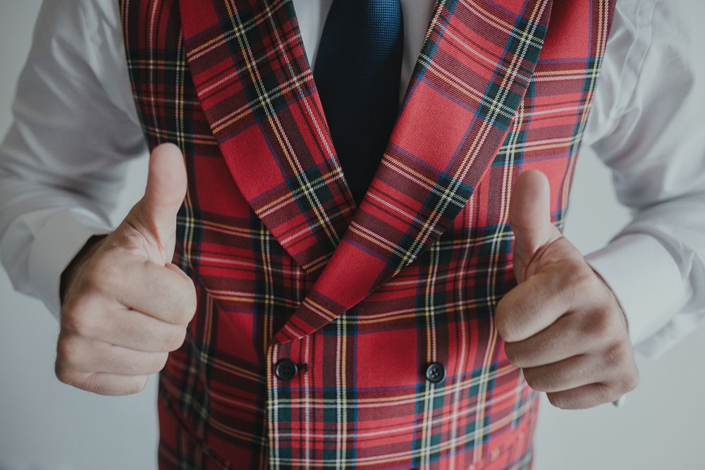 Person giving thumbs up while wearing red plaid waistcoat and white dress shirt.