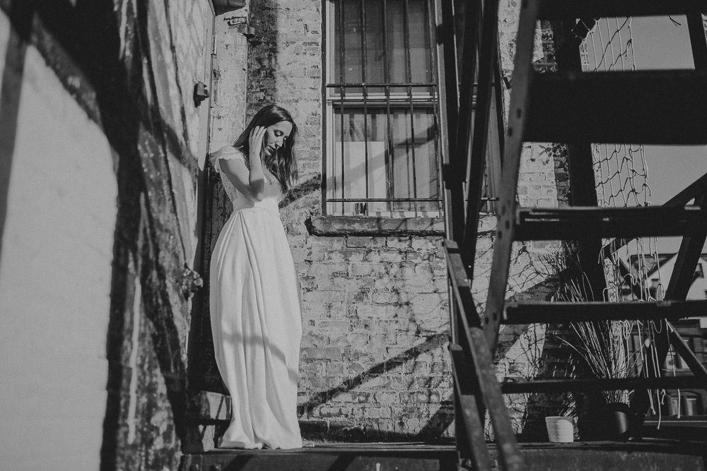 Black and white photo of flowing white dress on industrial fire escape stairs.