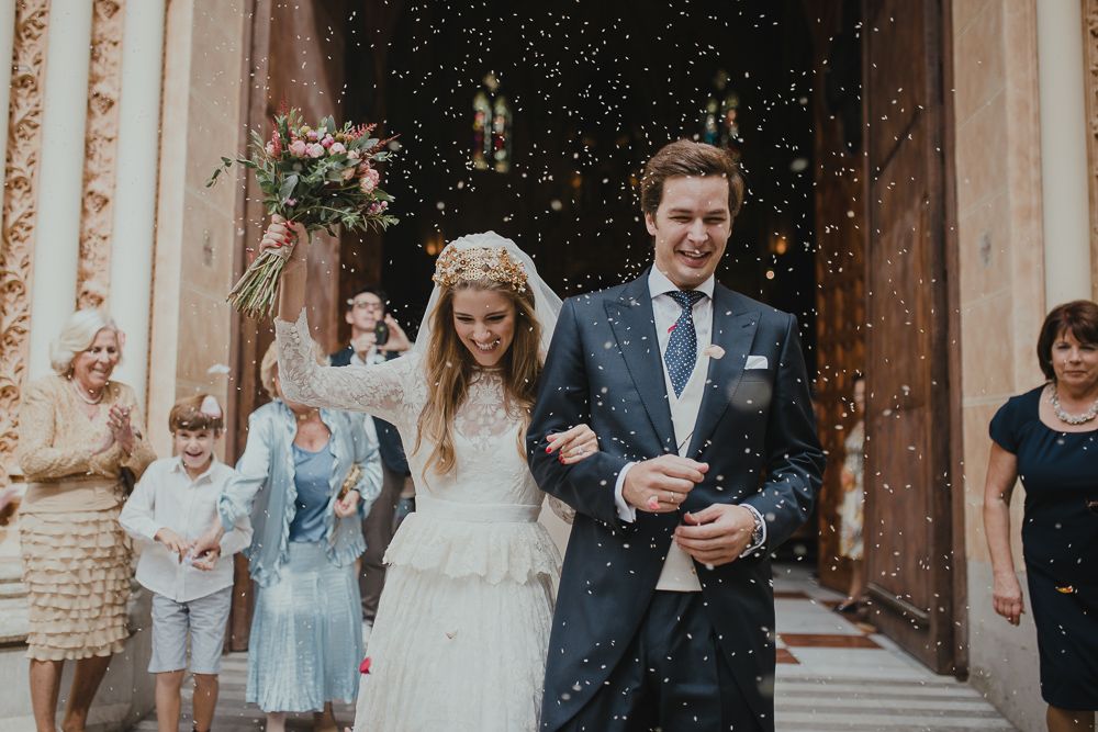Newlyweds exit church doors while guests throw confetti in celebration.