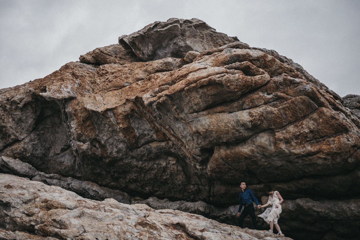 Two figures walking along dramatic rocky cliffs under stormy skies.