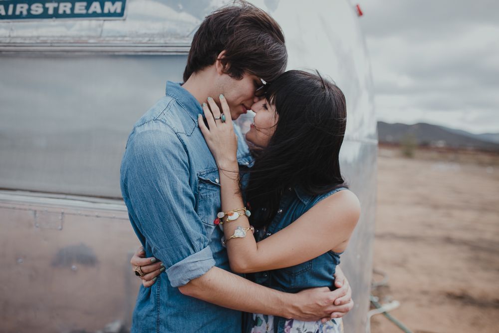 A couple embraces tenderly against the metallic surface of an Airstream trailer.
