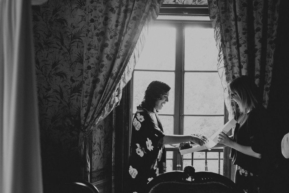 Two silhouettes by window with ornate curtains in black and white photography.
